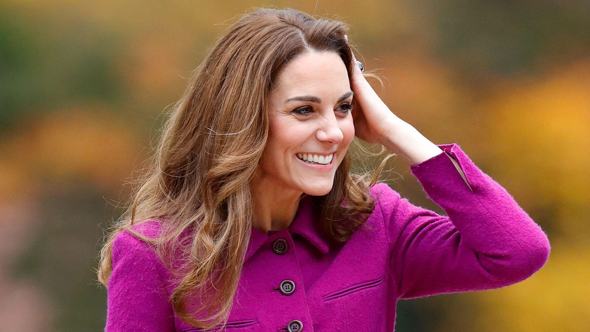 Kate Middleton touching her hair in a bright pink coat dress