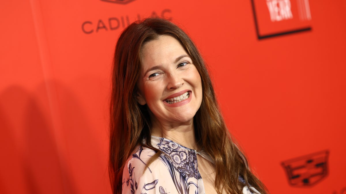 Drew Barrymore on the carpet in a patterned dress looks slightly behind her on the carpet