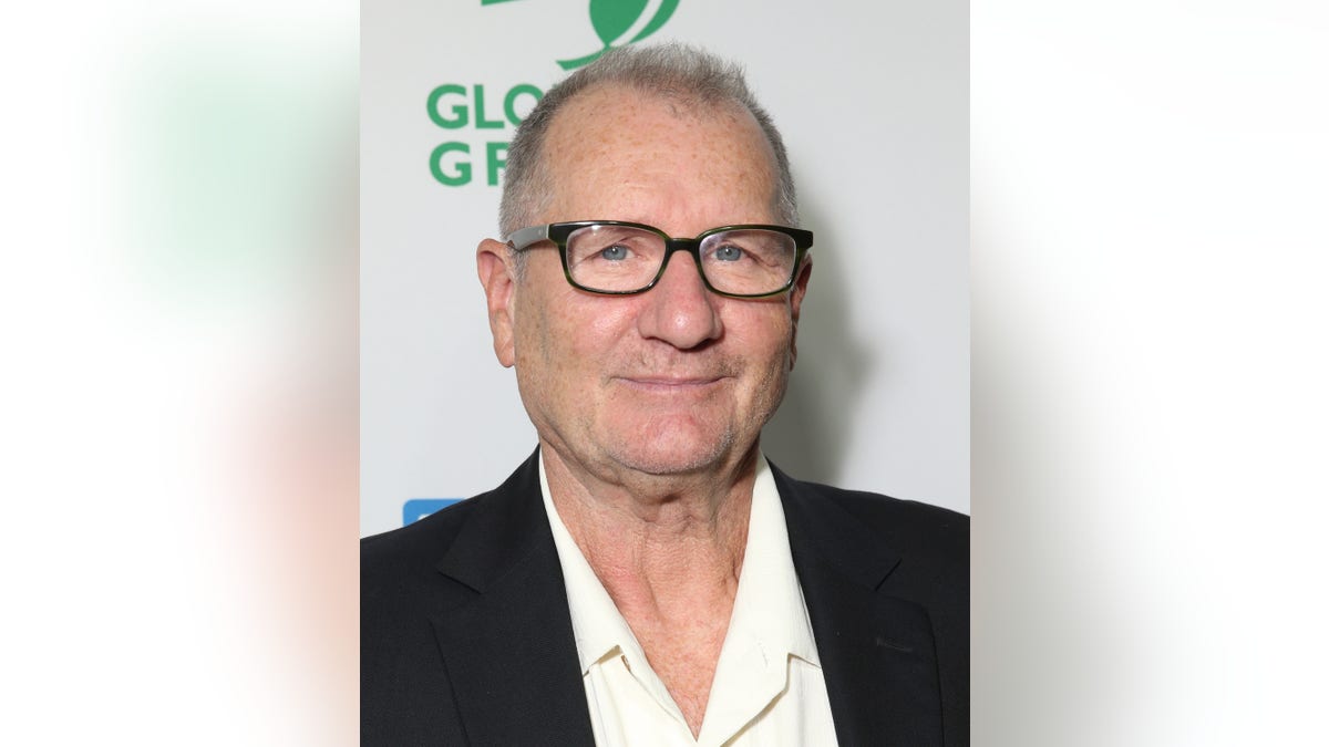 Ed O'Neill in a white shirt and black suit with dark frame glasses