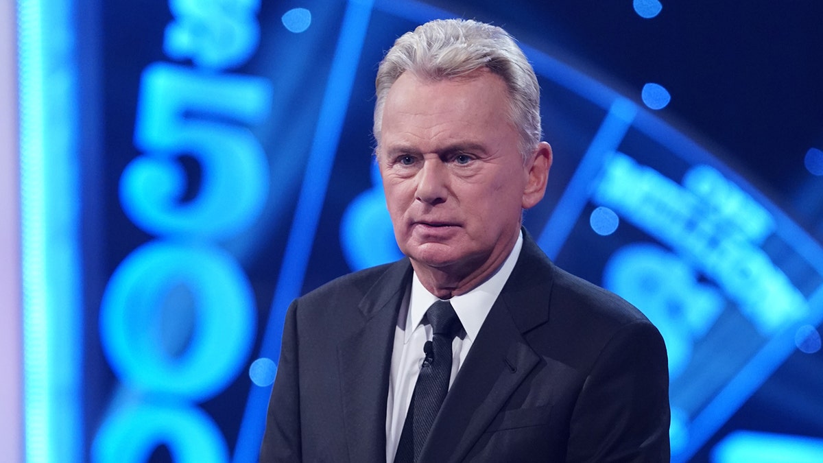 Pat Sajak looks confused in a suit on the set of "Wheel of Fortune"