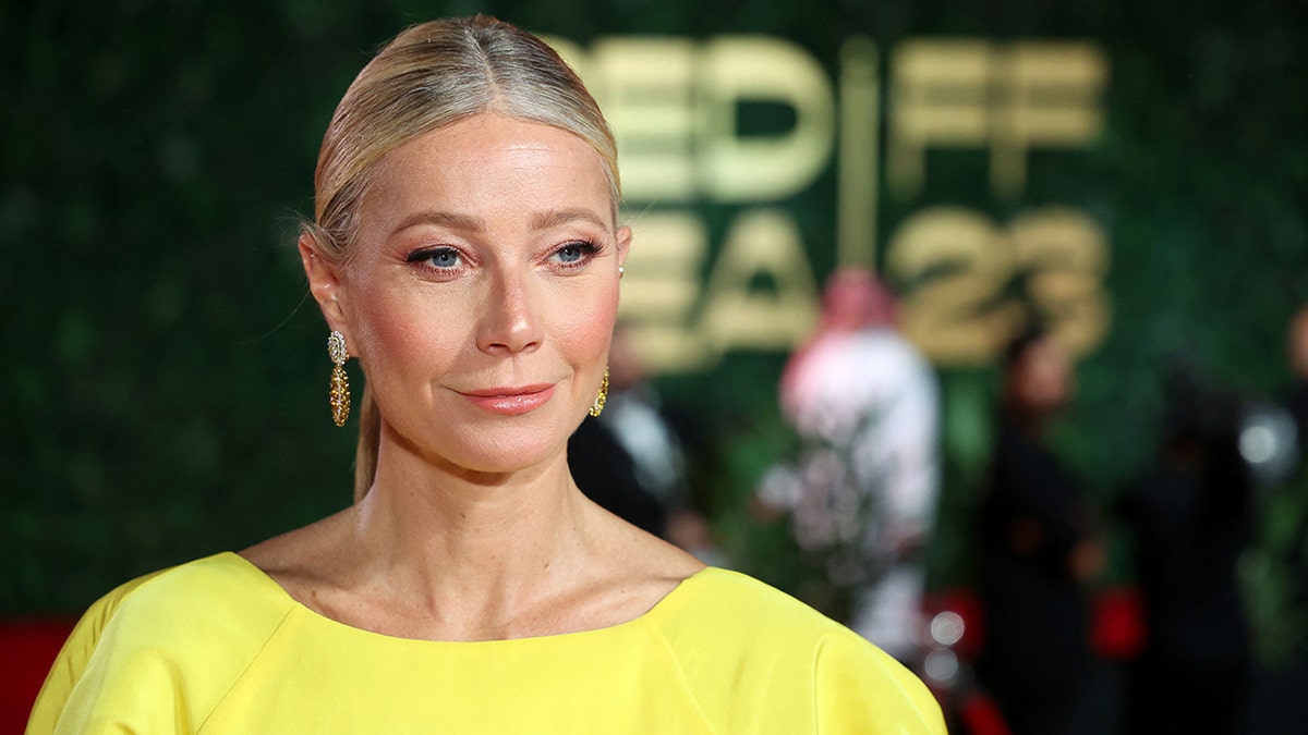 Gwyneth Paltrow in a yellow dress and dangly earrings looks to her left on the carpet