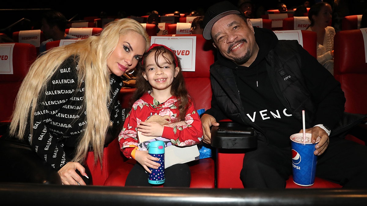 Coco Austin in a black Balenciaga sweater leans close to daughter Chanel in a movie theater with husband Ice T on the left of Chanel