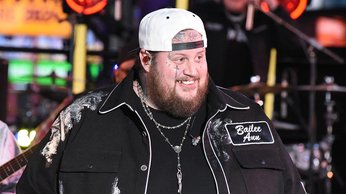 Jelly Roll in a black outfit with white trim and white backwards hat on stage in New York City