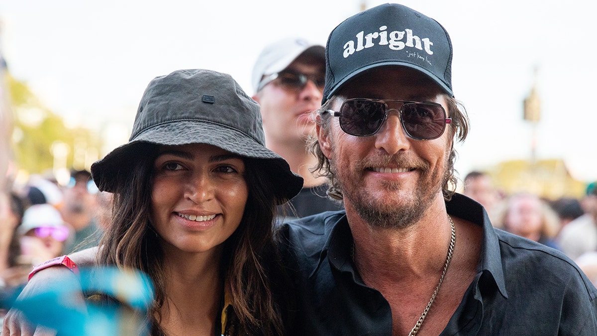 Camila Alves in a black bucket hat smiles with husband Matthew McConaughey in an 'alright' hat