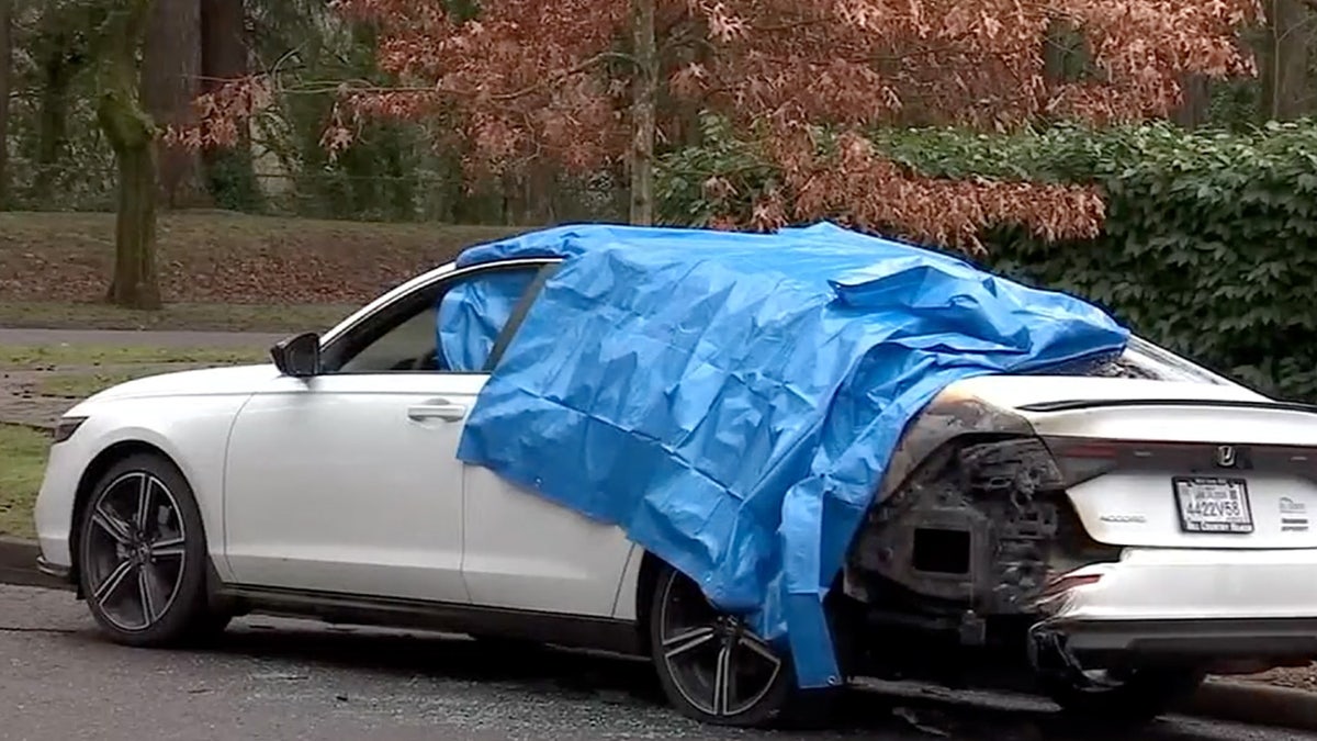 Blue tarp draped over a white car with a burned bumper