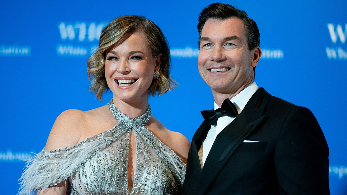 Rebecca Romijn in a halter dress with a cut-out smiles for a photo with husband Jerry O'Connell in a standard tuxedo
