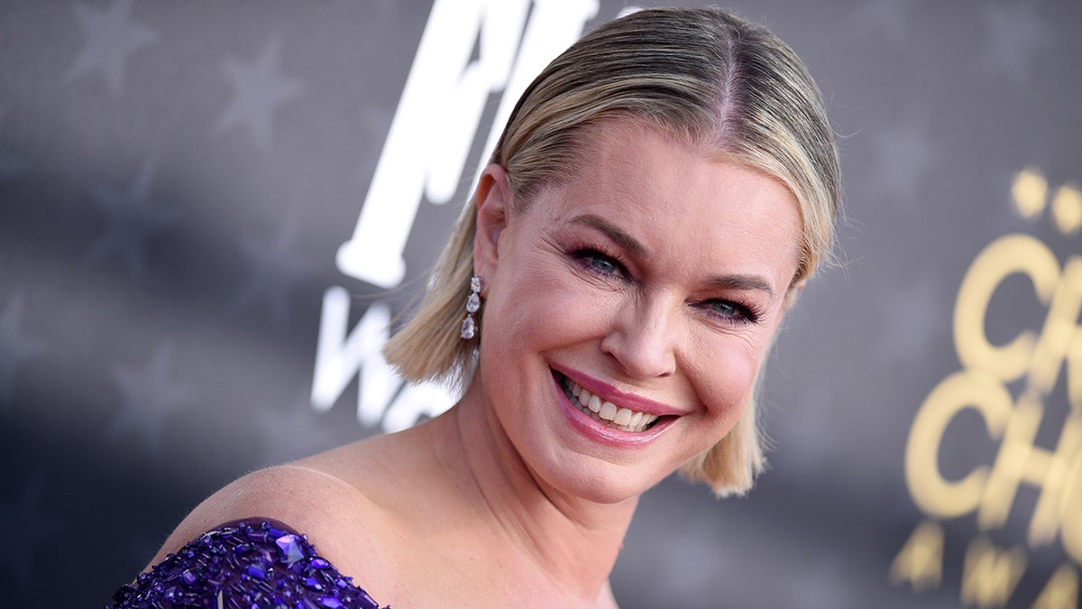 Rebecca Romijn smiles on the carpet at the Critics Choice Awards ina. purple sparkly dress