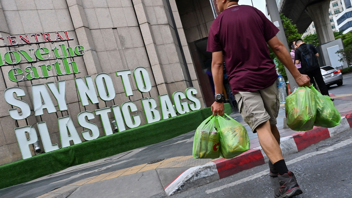 Man holds plastic bags while looking at 'say no to plastic bags' sign to his left