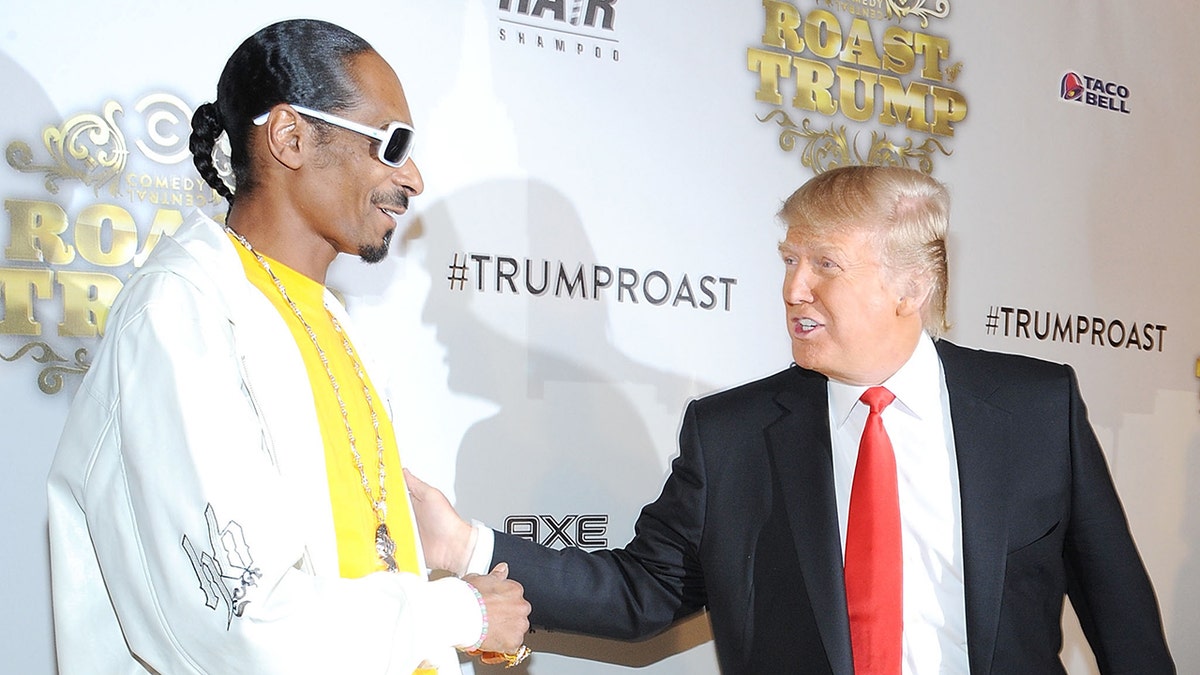 Snoop Dogg in a yellow shirt and white jacket speaks with Donald Trump on a carpet
