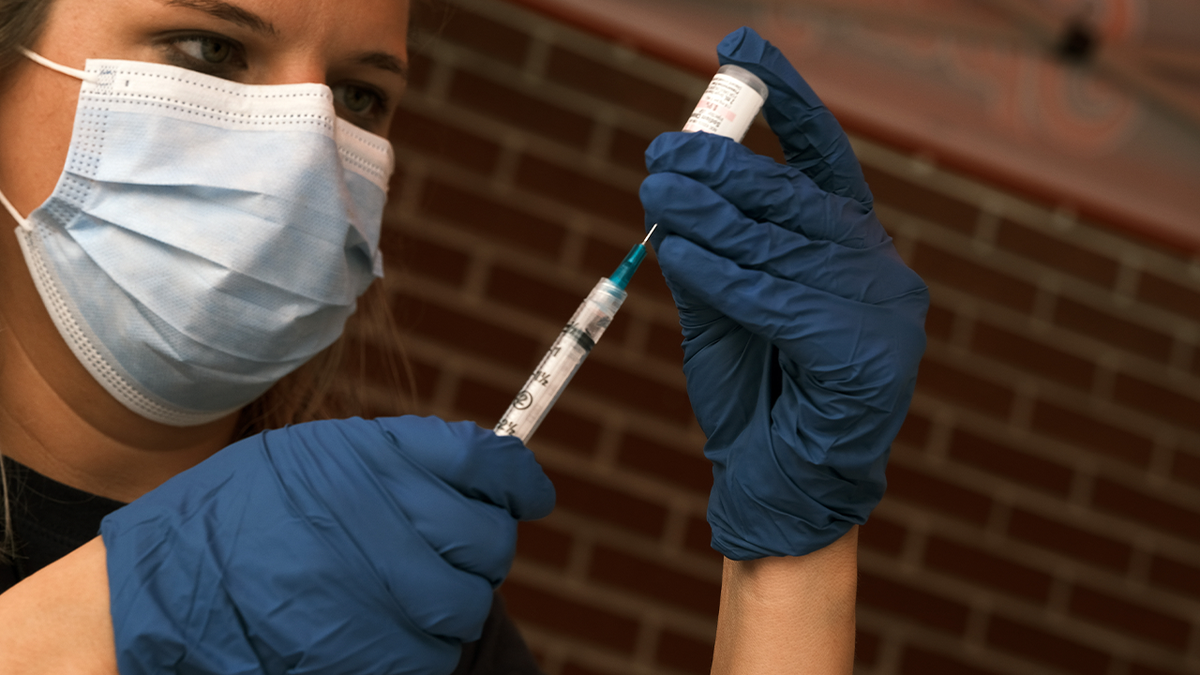 Woman in mask, gloves with syringe and vial