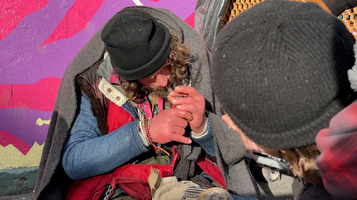 Man covered with wool blanket smokes out of a glass pipe in Portland, Oregon