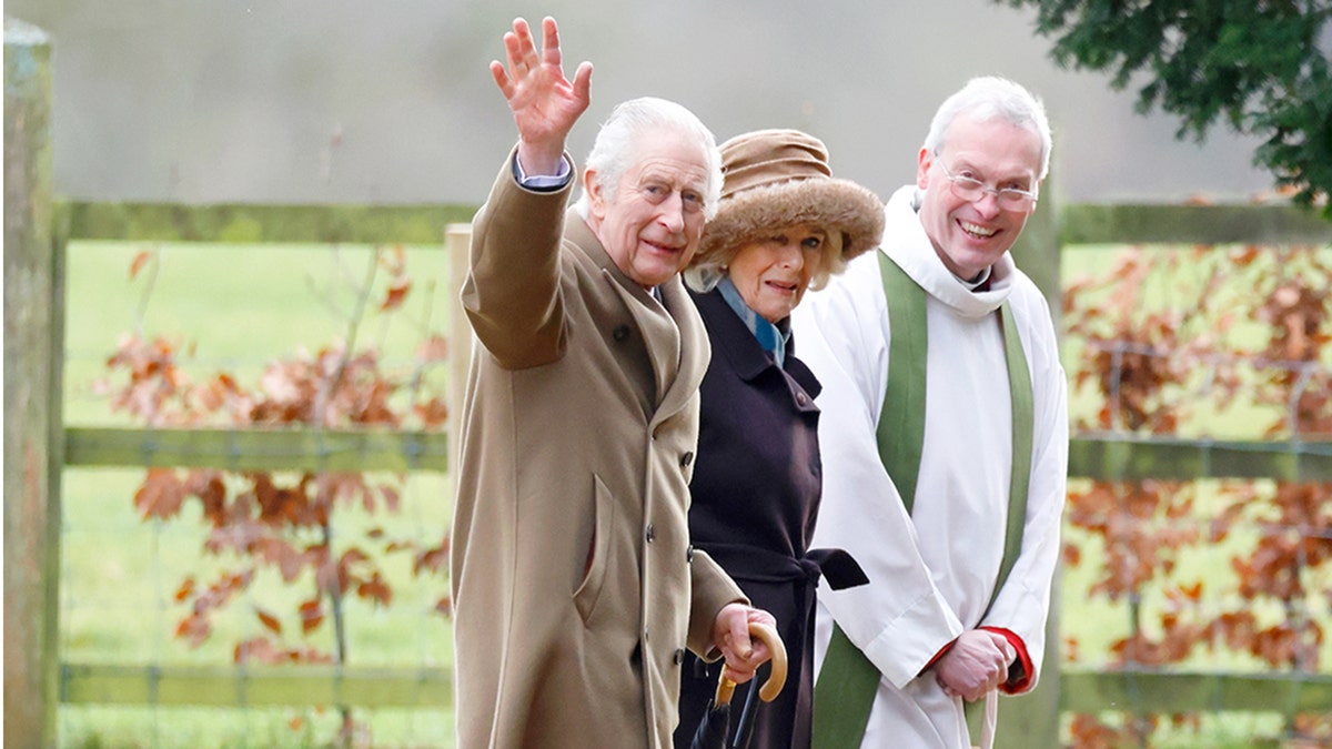 King Charles waves as he walks alongside Queen Camilla and The Reverend Canon Dr Paul Williams