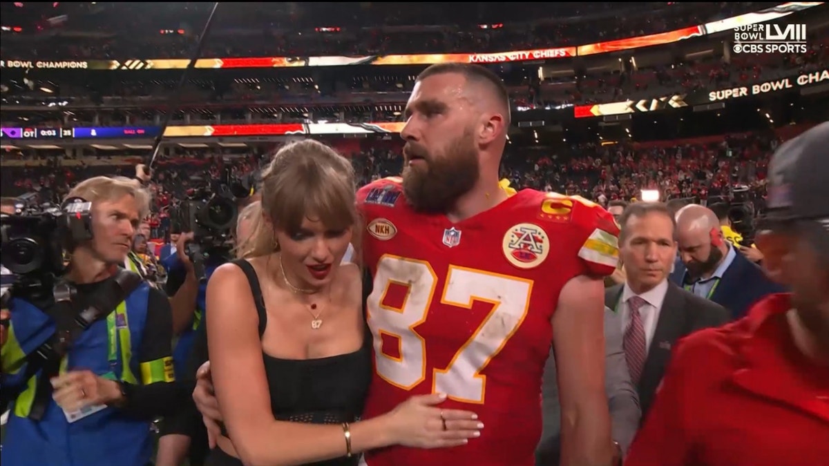 Taylor Swift e Travis Kelce se abraçam enquanto caminham em campo no Super Bowl