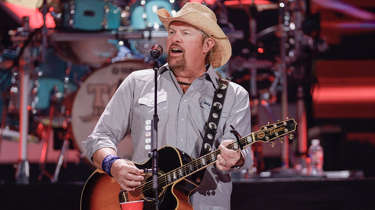 Toby Keith com um chapéu de cowboy bege toca violão no palco em Austin, Texas
