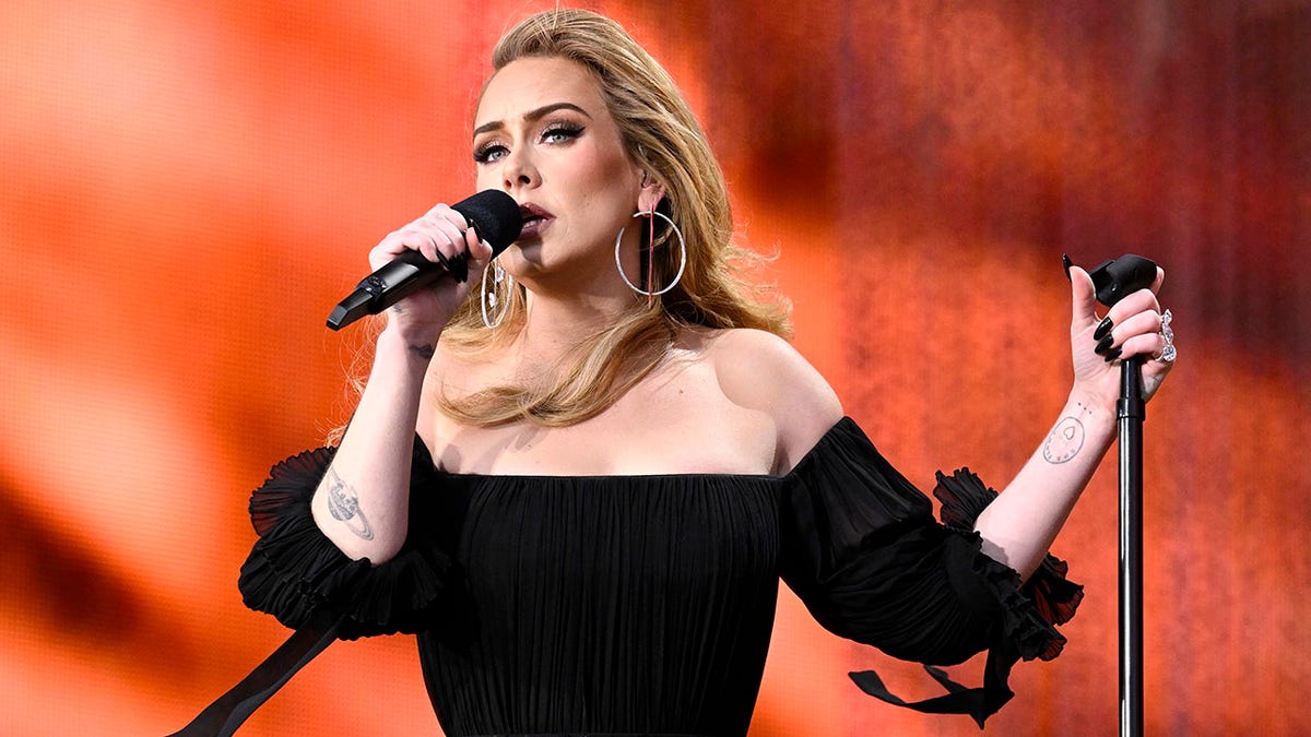 Adele looks out longingly into the crowd as she sings on stage in a black off the shoulder dress