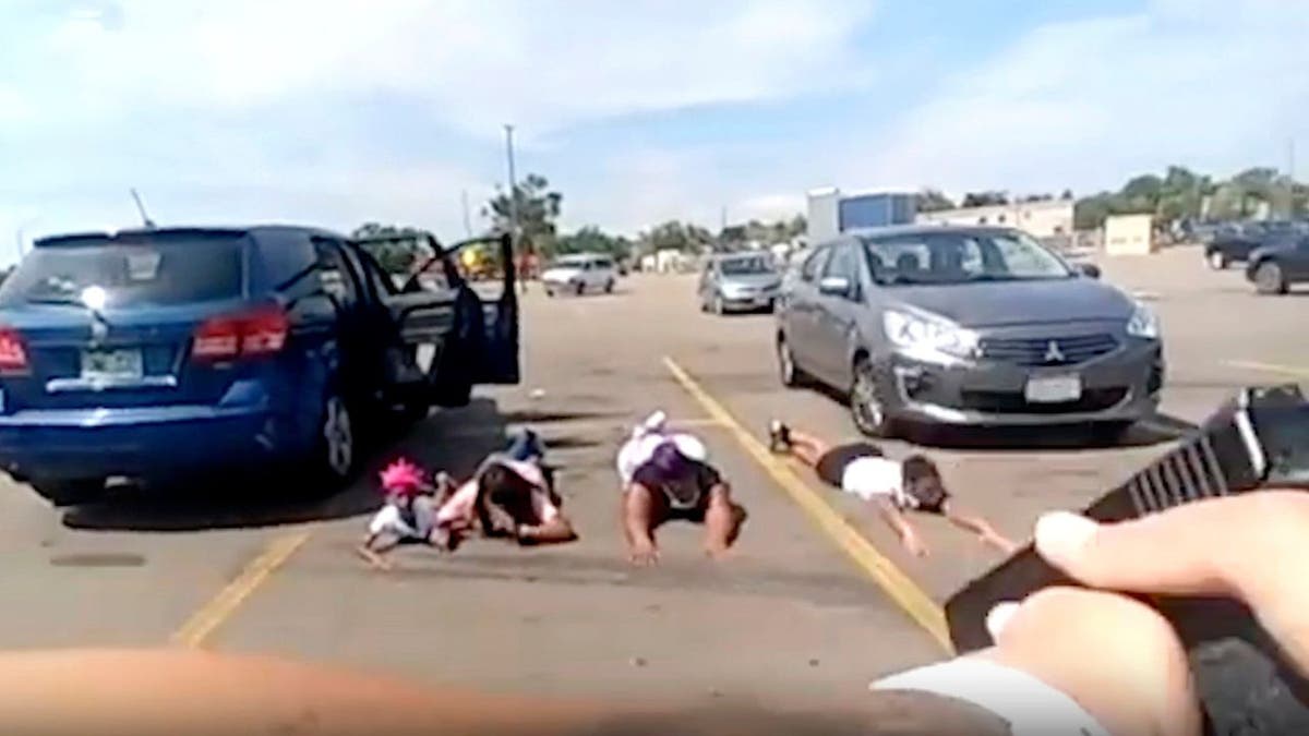 body cam screenshot of a police officer points his gun at four young girls lying facedown in a parking lot 