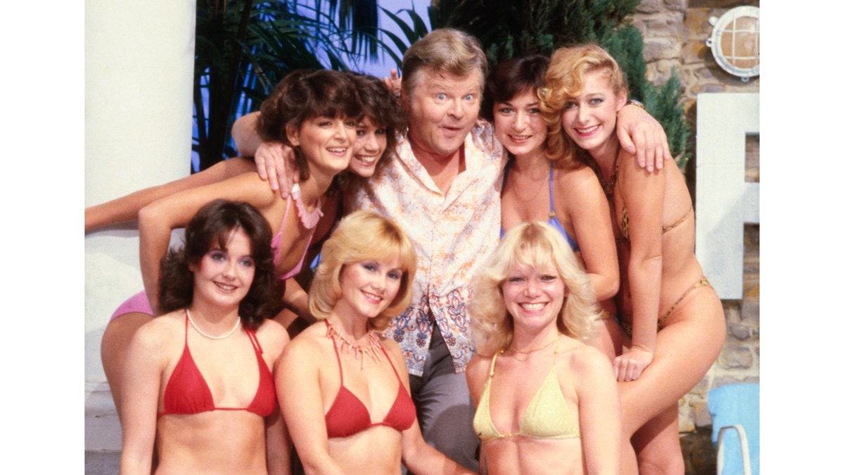 Benny Hill surrounded by seven women in bikinis