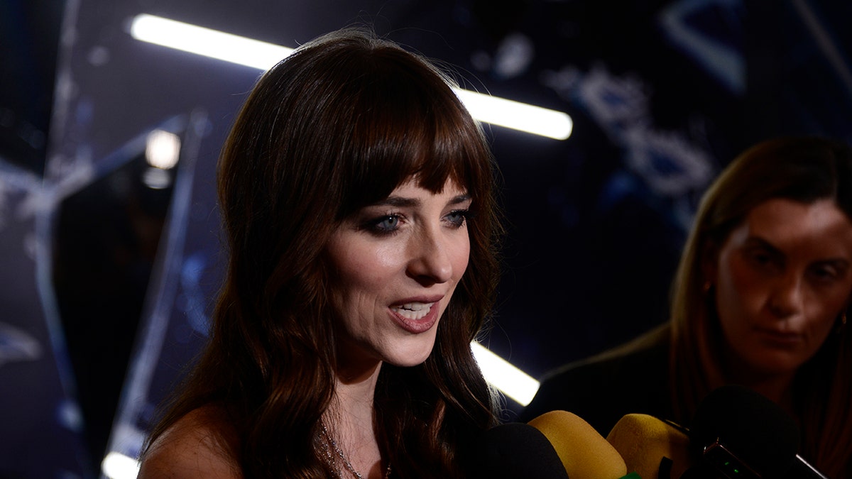 Dakota Johnson speaking into microphones on red carpet