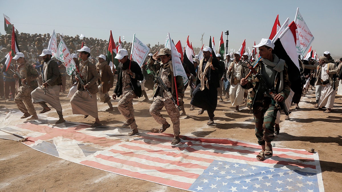 Houthi fighters are throwing stones at the US and UK flags.
