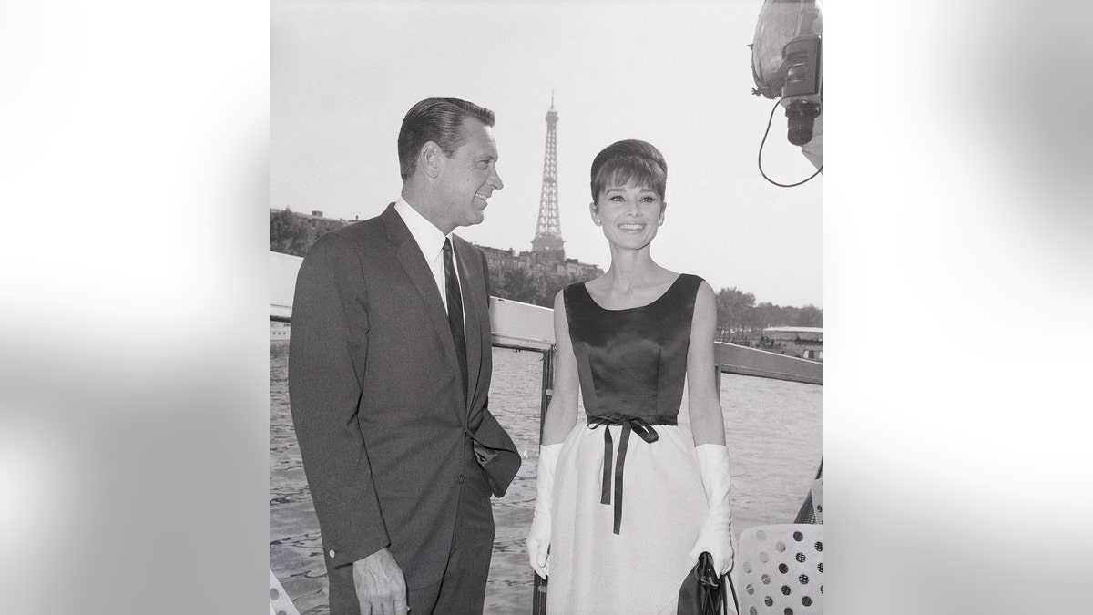 Audrey Hepburn smiling next to an actor with the Eiffel Tower behind them