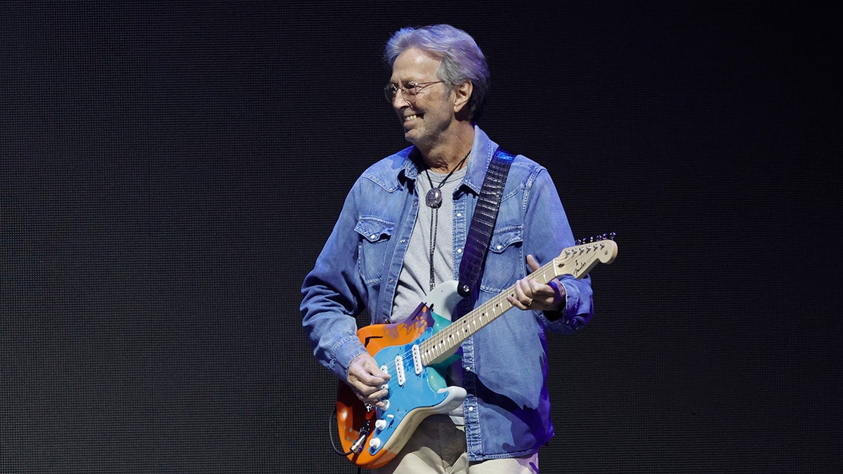 Eric Clapton holding a guitar and wearing a blue open shirt