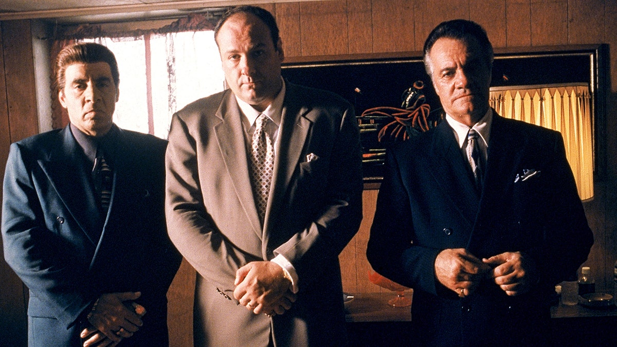 James Gandolfini standing in the center between two men as they play mobsters in front of cameras