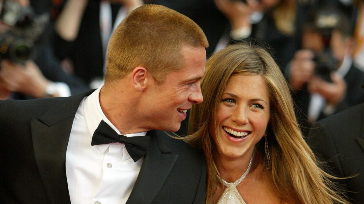 Jennifer Aniston smiling as Brad Pitt looks in her direction on the red carpet
