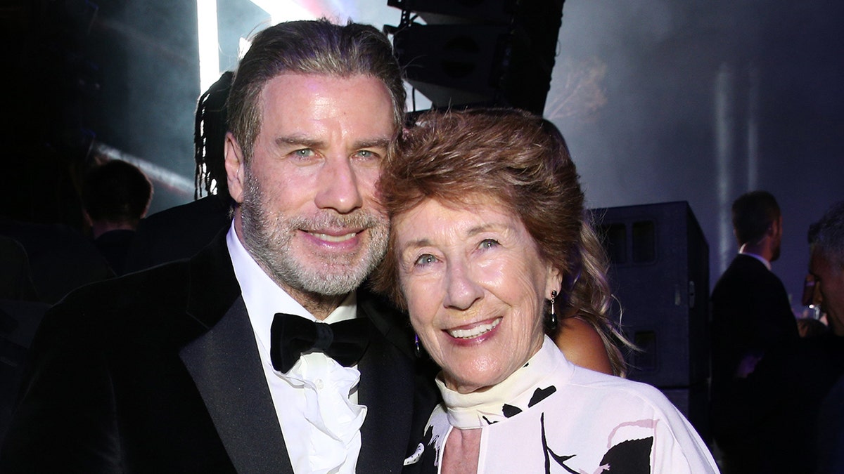 John Travolta wearing a suit and tux next to his sister Ellen Travolta in a white sweater dress