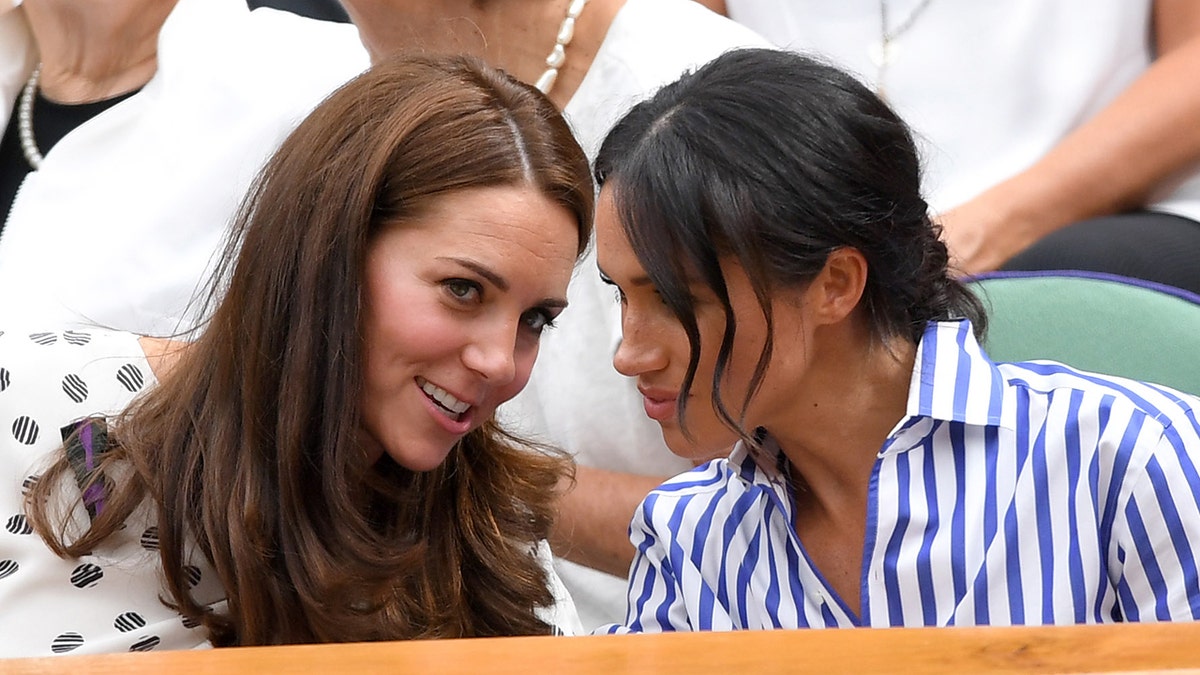 Kate Middleton and Meghan Markle leaning into each other and talking