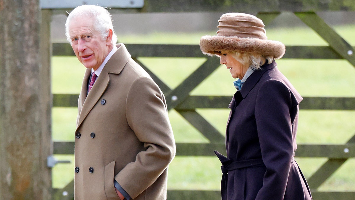 King Charles wearing a brown coat walking next to Camilla