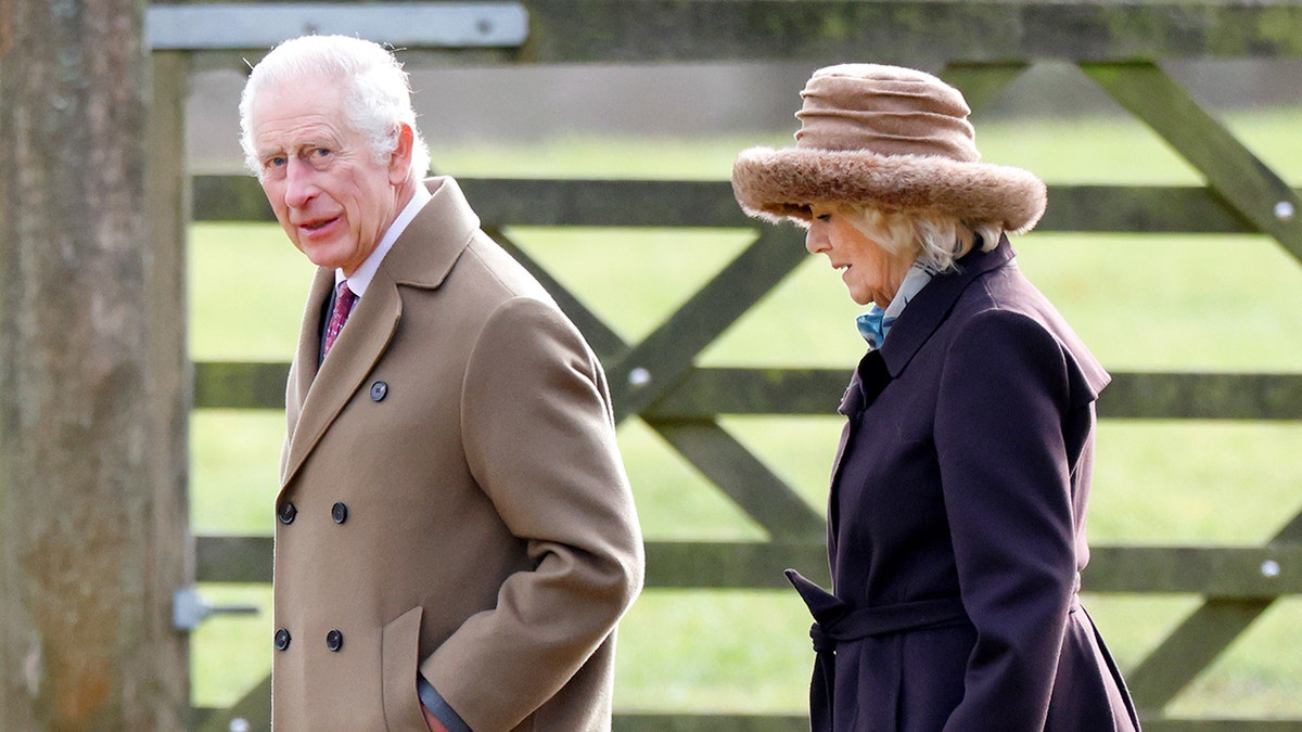 King Charles in a brown coat next to Queen Camilla
