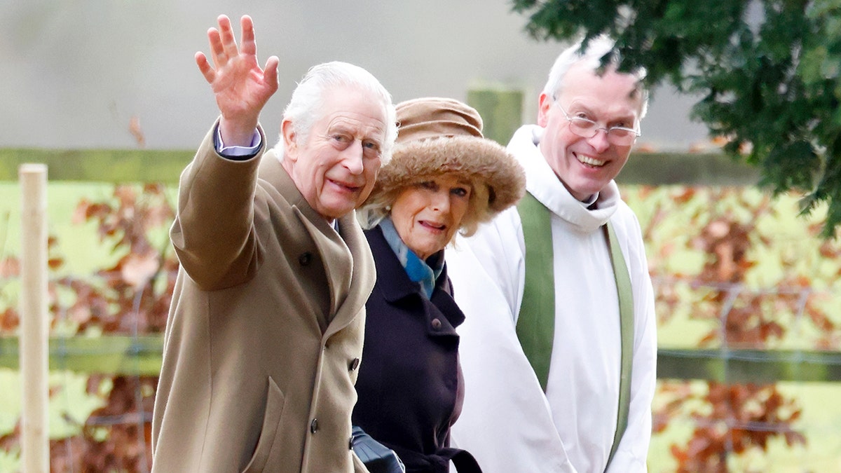 Koning Charles zwaait naast koningin Camilla en een priester