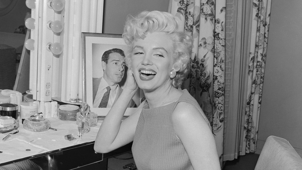 Marilyn Monroe smiling next to a portrait of Joe DiMaggio