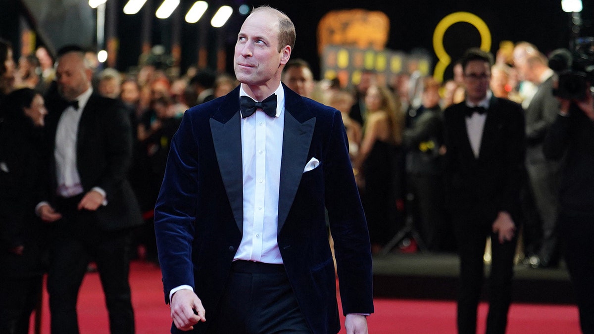 Prince William wearing a suit and bow tie walking on the red carpet