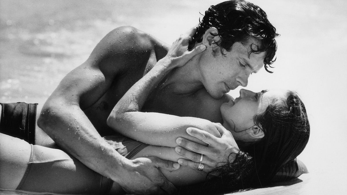 Susan Lucci being embraced by an actor on the beach as she plays Erica Kane