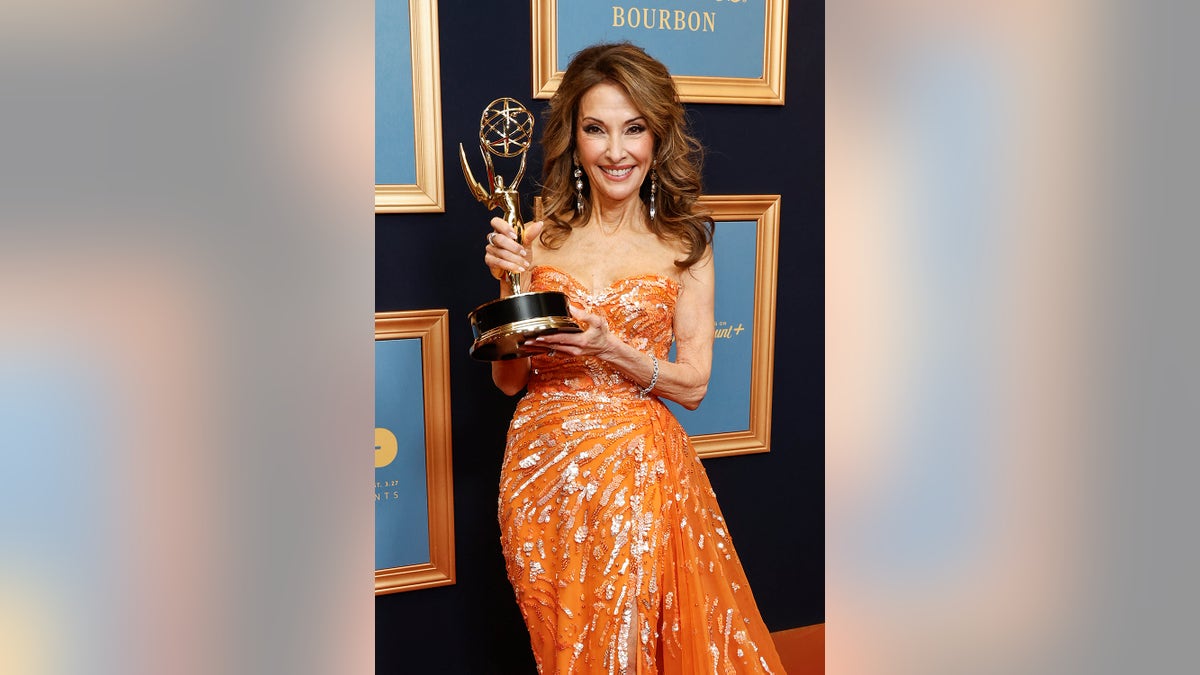 Susan Lucci wearing an orange dress and holding an Emmy
