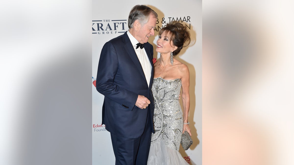 Susan Lucci wearing a strapless silver dress being admired by her husband in a suit