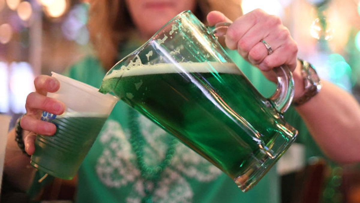 A woman pours green beer from a jug