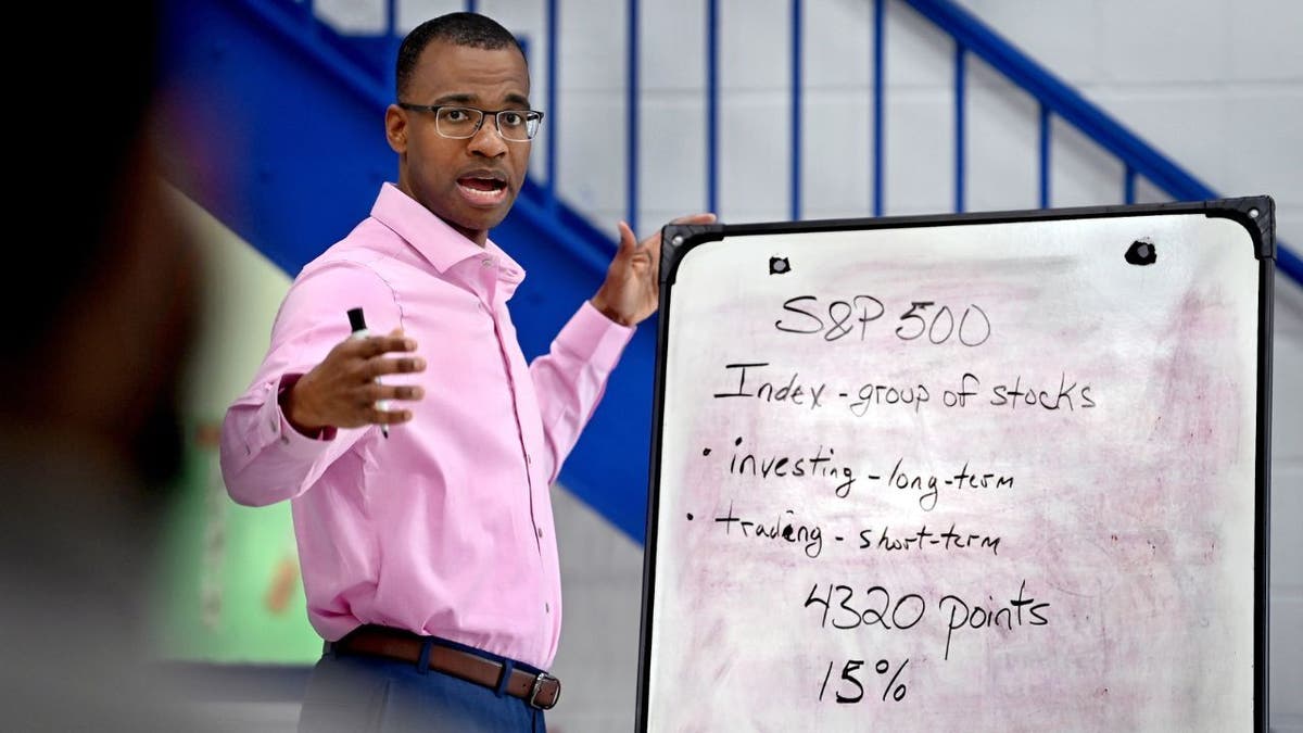 Joel Castón speaking, wearing a pink polo shirt, standing next to dry erase board with information written on it