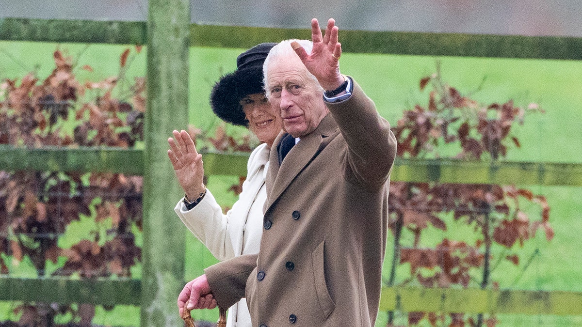 Rei Carlos III acena para espectadores caminhando com a Rainha Camilla