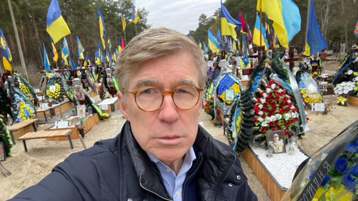 Fox News' Greg Palkot pictured up close with cemetery and flags behind him in Kyiv
