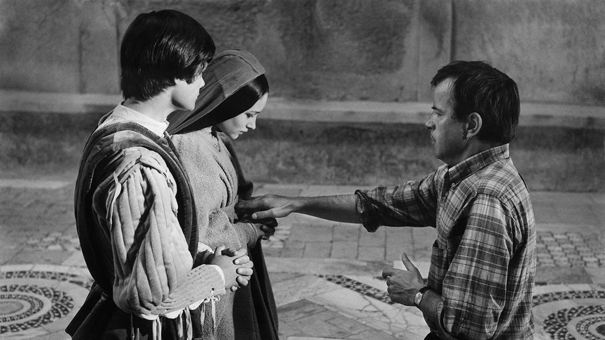Black and white photo of Leonard Whiting and Olivia Hussey being directed by Franco Zeffirelli