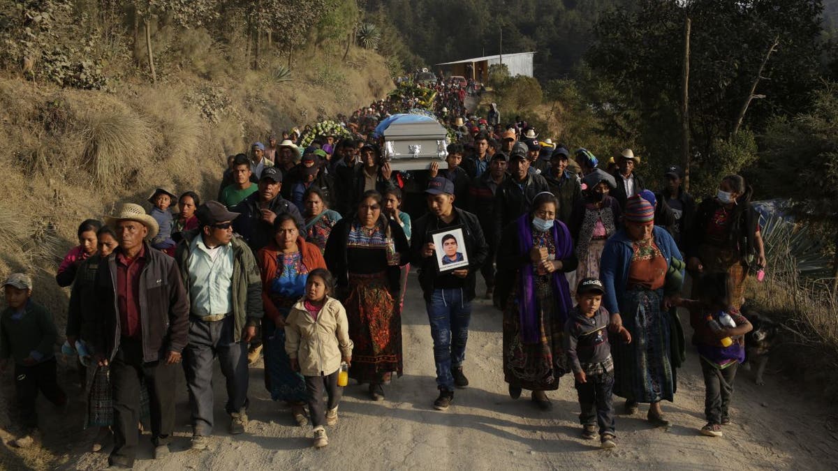 Dozens of people walk alongside a coffin in Guatemala