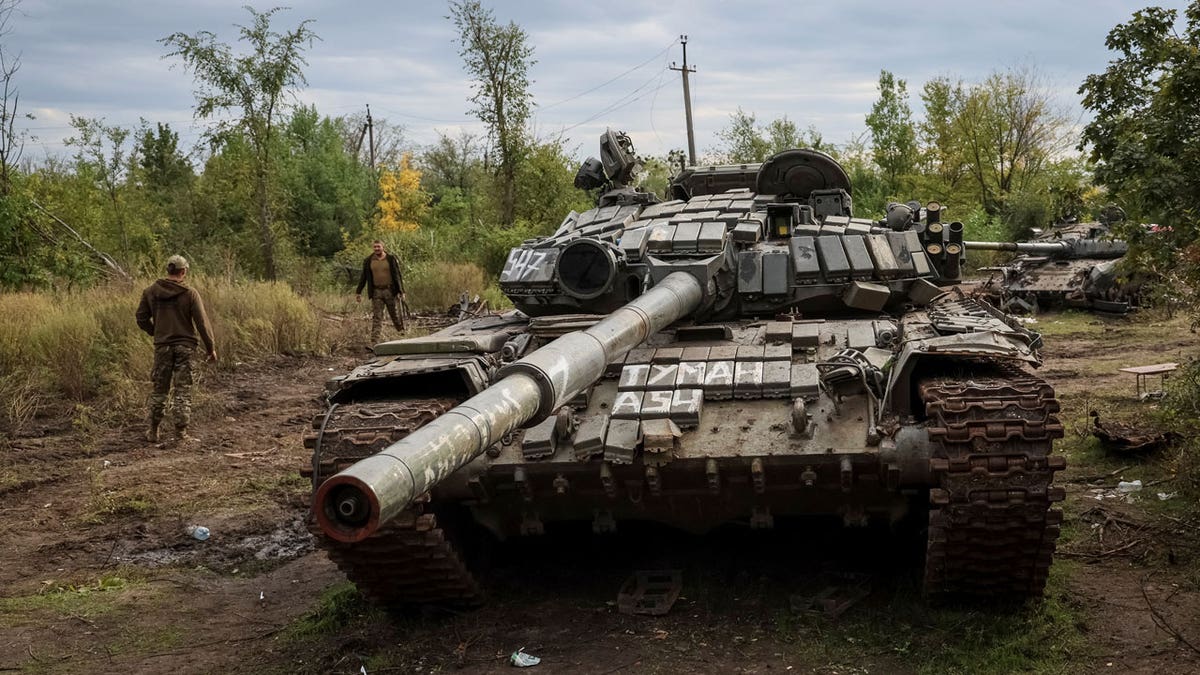 Ukrainian servicemen walk near destroyed Russian tanks
