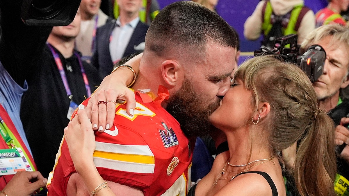 Travis Kelce em seu uniforme vermelho do Chiefs beija Taylor Swift em campo após vencer o Super Bowl