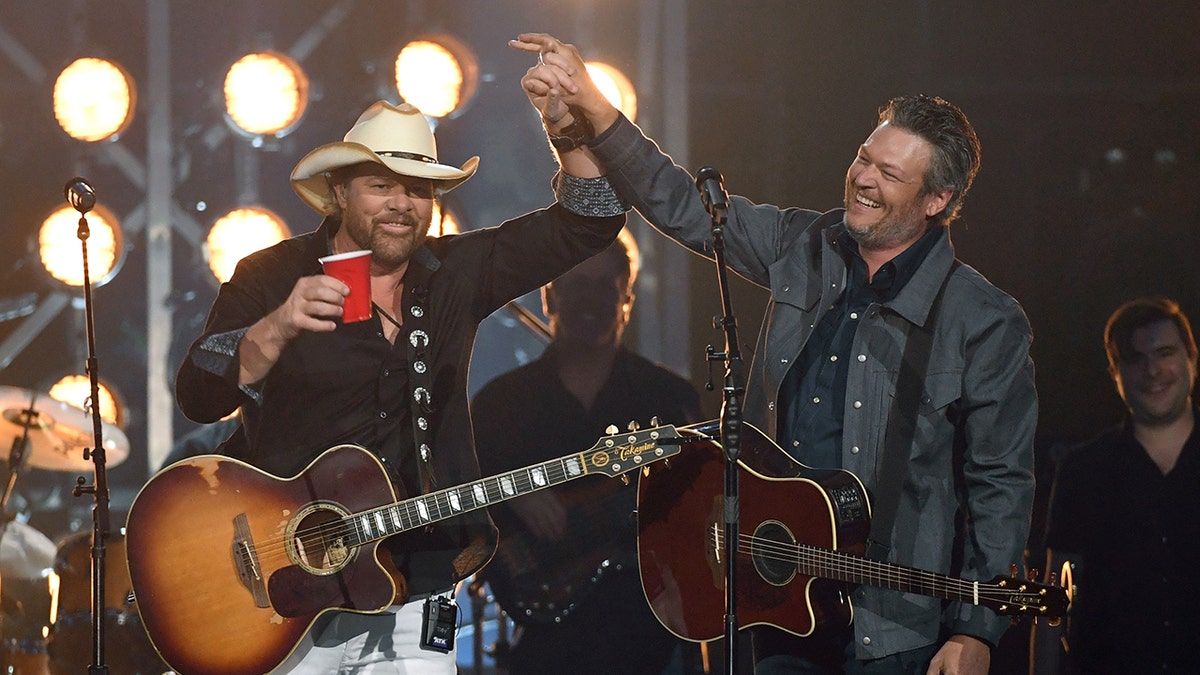 Toby Keith standing on stage with Blake Shelton, holding hands