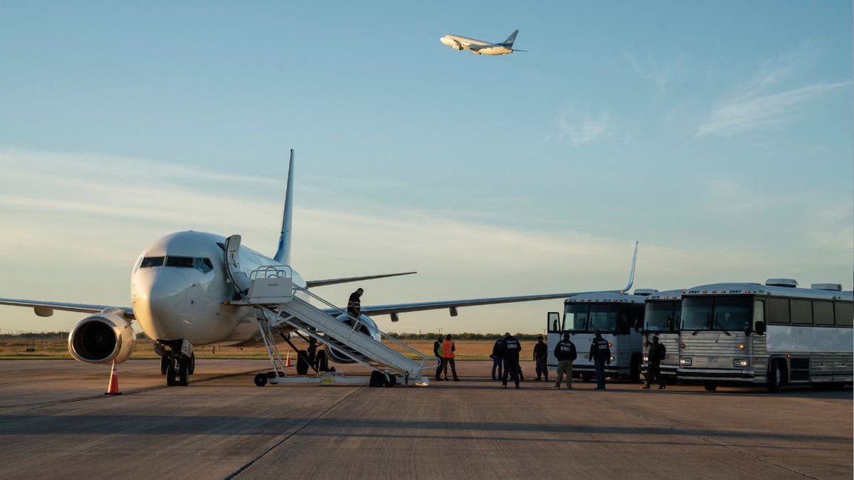 Migrants boarding a deportation flight with three buses next to a plane