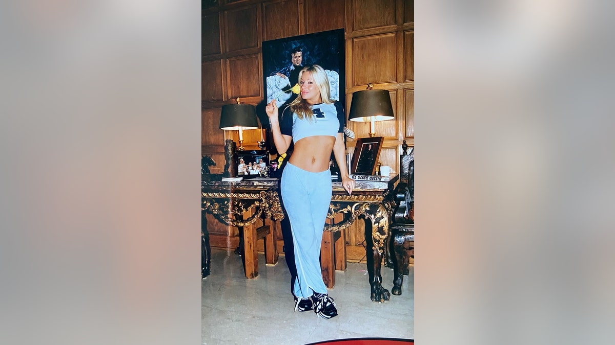 Zoe Gregory wearing a matching blue shirt and pants with her arms raised at the Playboy Mansion