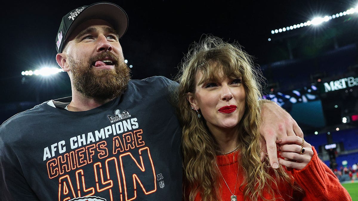Travis Kelce on the field with his tongue hanging out slightly puts his arm around Taylor Swift after winning the AFC Championship game