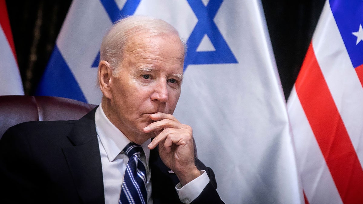 Biden com a mão até os lábios sentado em frente à bandeira de Israel